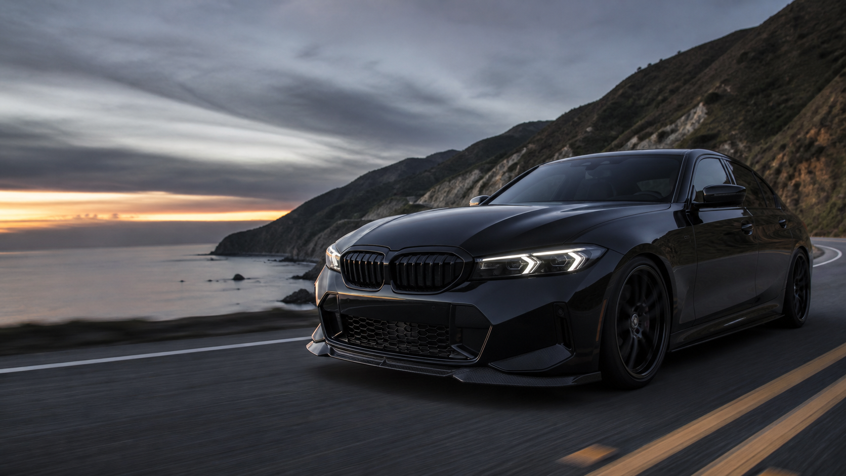 Black performance sedan driving on a coastal road